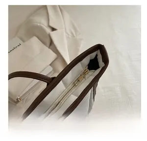 Detailed close-up of smooth gold metal zipper and brown leather trim on a quilted tote bag
