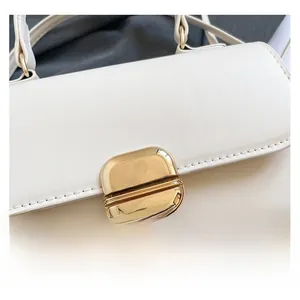 Close-up of white leather handbag featuring a polished gold metal twist-lock and fine stitching