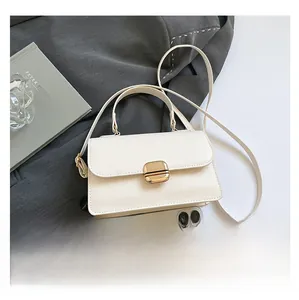White minimalist crossbody bag with gold buckle shown next to a phone for size comparison