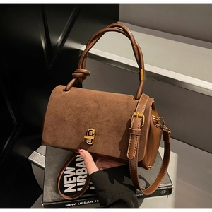 Detail of a brown suede handbag with knotted handle design and golden twist lock
