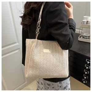Close-up of woven straw tote bag featuring a leather chain strap and brand label detail
