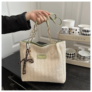 Detail of woven straw tote bag with green leather trim and gold chain handle