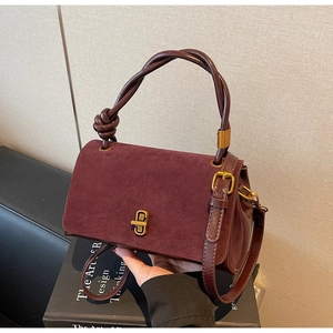 Detail of burgundy suede leather handbag featuring gold twist lock and knotted handle