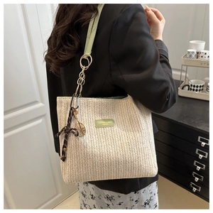Detail of woven straw tote bag with green leather strap and tennis racket pendant decor