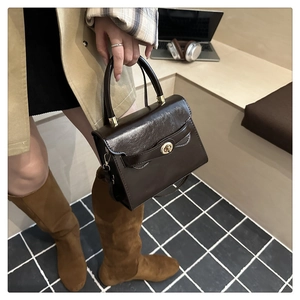 Dettaglio di borsa in pelle cioccolato con patta a onde e chiusura a girello dorata