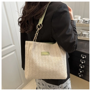 Close-up of woven tote bag with green leather strap and gold chain detail on model