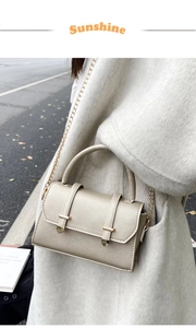 Détail du sac à bandoulière champagne en cuir grainé avec finitions dorées sur un manteau