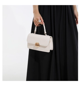 Detail of cream white leather handbag featuring a square gold metal lock and top handle
