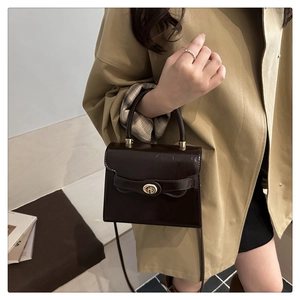 Detail showing the glossy dark brown leather surface and gold hardware of the handbag