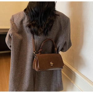 Detail of dark brown suede and leather crossbody bag featuring a knotted handle and metal lock