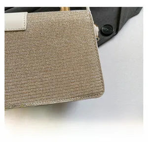 Detail of gold metallic woven fabric texture and white leather trim on small square bag
