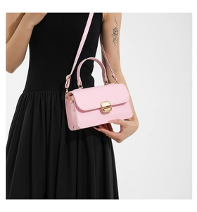 Detailed view of a pink faux leather square bag with gold hardware worn by a model