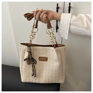 Detail of woven straw tote bag with brown leather handles and a striped pendant charm