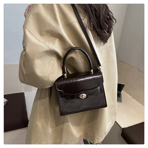 Detail of dark brown leather handbag with gold metal clasp on a beige coat outfit