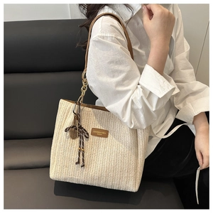 Detail of hand-woven straw tote bag with brown leather tag and chain handle