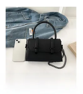 Sac bandoulière minimaliste en cuir noir posé à côté d'un smartphone pour comparer la taille