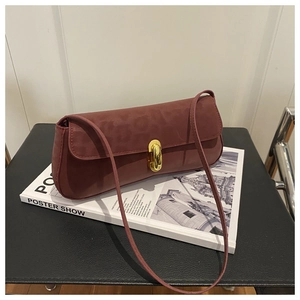 Dettaglio di una borsa a spalla in pelle bordeaux con chiusura dorata su rivista