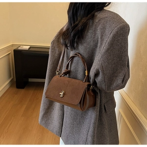 Close-up of brown faux suede flap and smooth leather body with golden twist lock