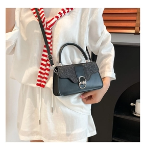 Detail of black glitter sequin box bag with silver clasp worn by model in white outfit