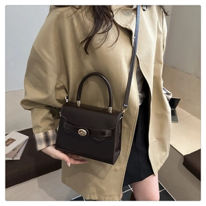 Detail of dark brown glossy handbag with vintage gold turn-lock and adjustable strap
