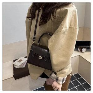 Detail of dark brown glossy leather handbag featuring elegant golden twist lock and top handle