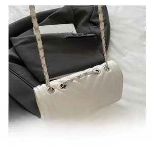 Detail of white quilted crossbody bag with metal chain strap and eyelet design