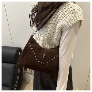 Dettaglio della borsa in pelle scamosciata marrone con borchie, croce e lunghe nappe