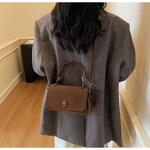 Close-up of brown suede crossbody bag with gold twist lock and knotted handle detail
