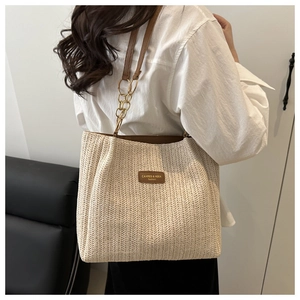 Detail view of woven straw tote bag featuring brown leather straps and gold metal hardware