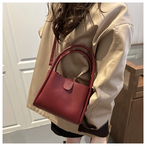 Detail of burgundy bucket bag worn by model showing smooth leather and ring handles