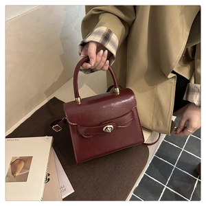 Detail of burgundy leather handbag featuring a vintage metal twist lock and sturdy handle