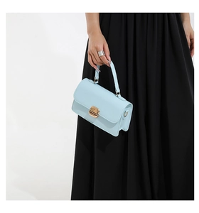 Detail of light blue crossbody bag featuring a golden magnetic clasp and textured leather