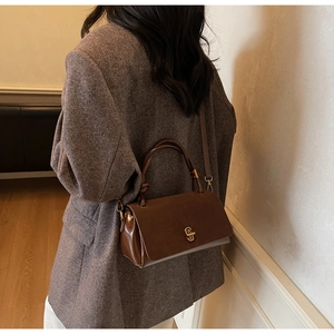 Detail of suede and patent leather patchwork handbag with gold metal clasp and thin strap