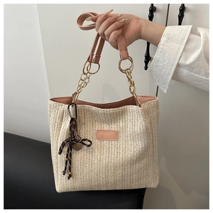 Detail of woven straw tote bag featuring pink leather straps and golden chain link