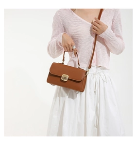 Close-up of caramel leather handbag with gold hardware worn with pink cardigan