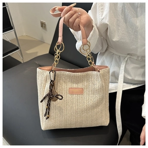 Close-up of woven straw tote with pink leather handle and gold badminton racket charm
