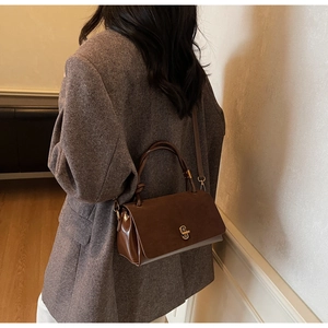Detailed side view of a brown suede and leather crossbody bag with gold metal twist lock