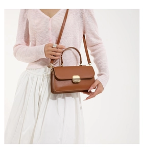 Close-up of brown leather square bag with gold buckle on a model's arm and shoulder