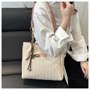 Detail of woven straw tote bag featuring pink leather straps and a decorative bow charm
