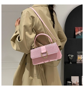 Detailed view of a pink rhinestone handbag with a gold horseshoe clasp on a model
