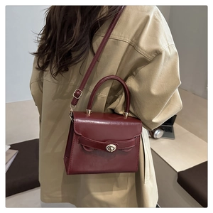 Burgundy faux leather crossbody bag with gold twist lock shown on a model's arm