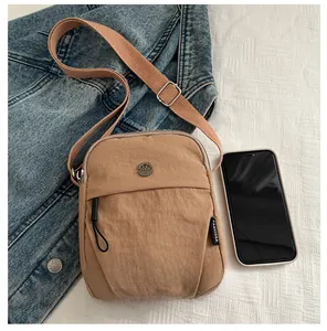 Detailed view of khaki nylon crossbody bag shown with a smartphone for size reference