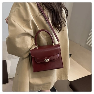 Detail of burgundy crossbody bag featuring a silver metal twist lock and matte PU texture