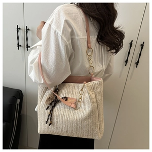 Close-up of woven straw tote texture with pink leather trim and silk scarf detail