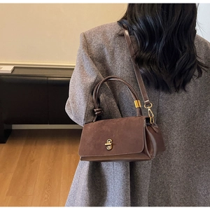 Detail of vintage brown suede handbag with metal clasp and unique knotted handle on model