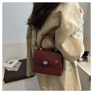 Detail of burgundy leather handbag with metallic twist lock and adjustable shoulder strap