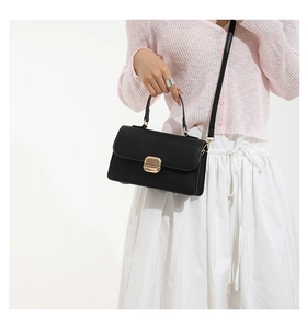 Detail of minimalist black handbag featuring a golden rectangular twist lock and top handle