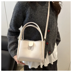 White minimalist bucket bag with top handles and shoulder strap shown on a model