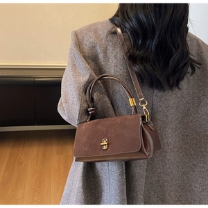 Detail of suede textured handbag with golden twist lock and smooth leather handle contrast