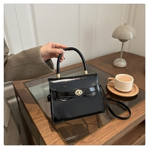 Detail of a black glossy trapezoid handbag with gold rotary lock on a wooden desk